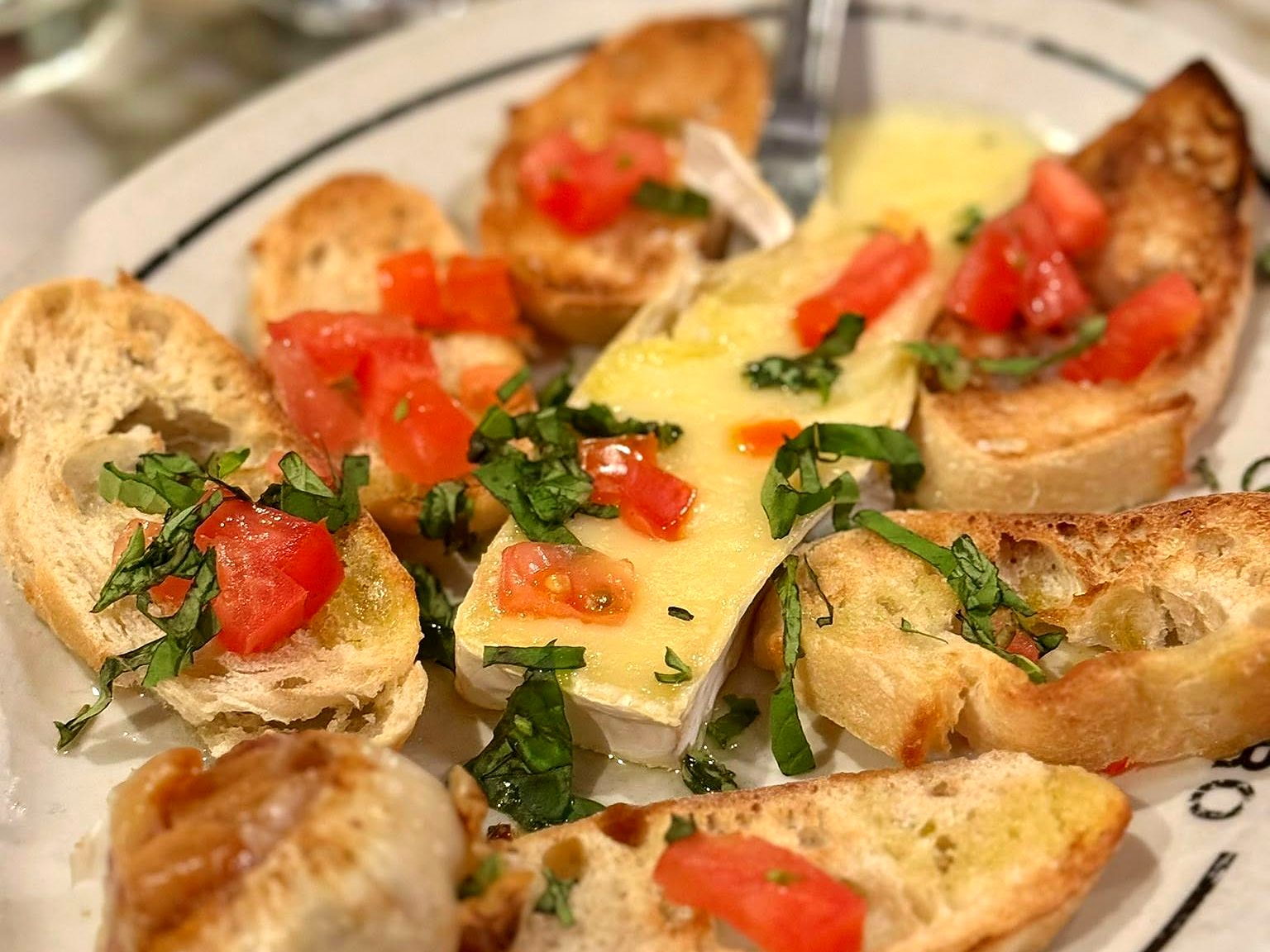 Baked brie at Aixois — a molten wedge ringed by crostini with bruschetta tomatoes, basil, and a whole head of roasted garlic.