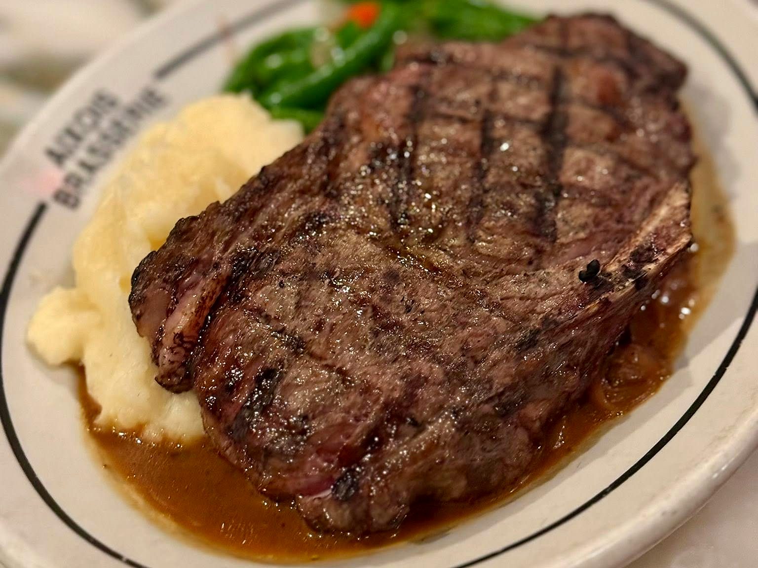 A grilled steak at Aixois — cross-hatched and resting in jus alongside pommes purée and haricots verts.