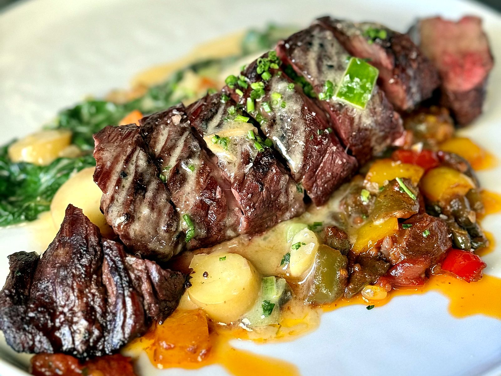 The grilled prime hanger steak at Osteria Bianchi, sliced over potato pavé and pepper relish with creamed greens.