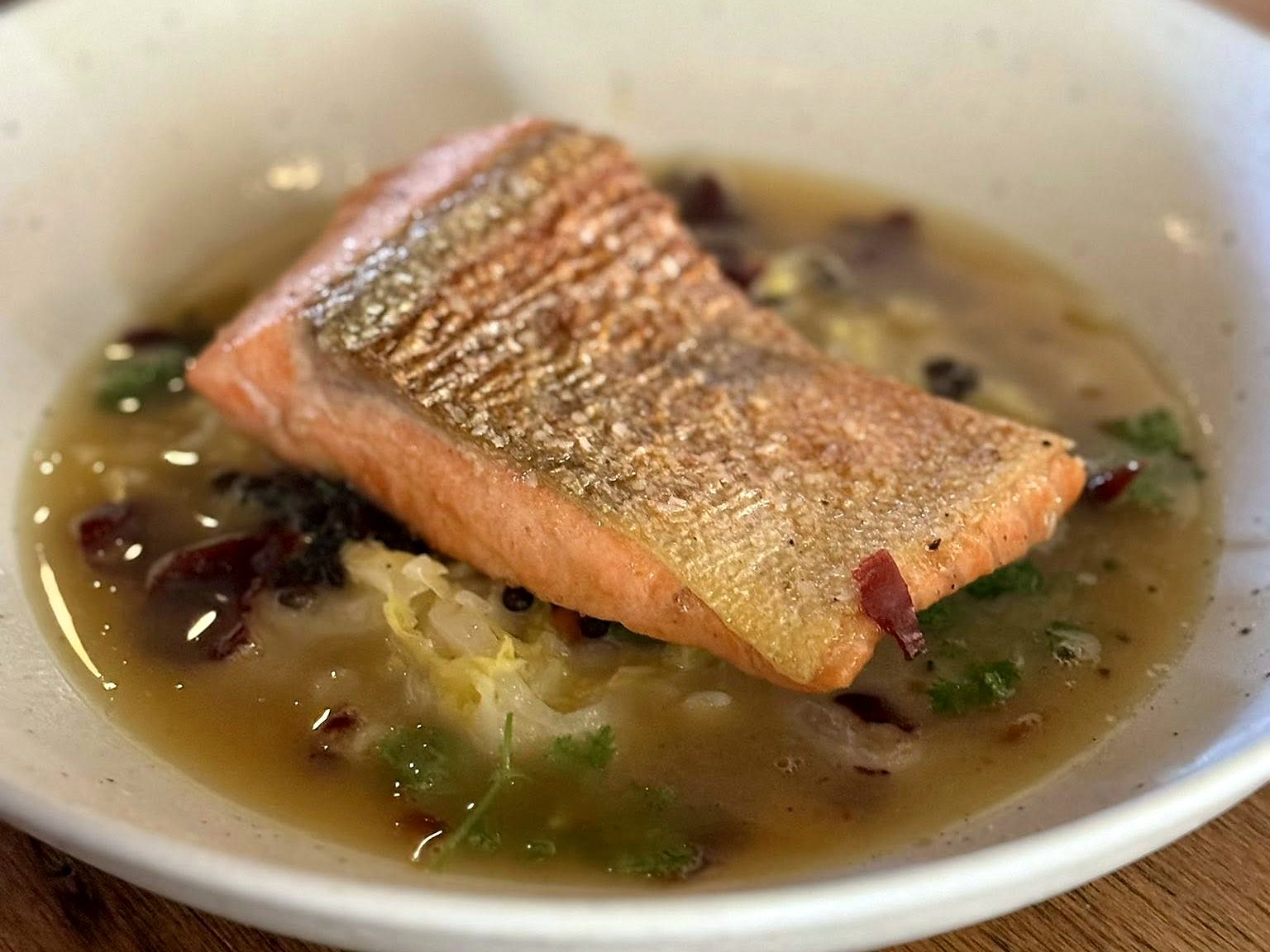 Crispy-skin salmon at Osteria Bianchi — a seared fillet on braised cabbage in a golden broth.