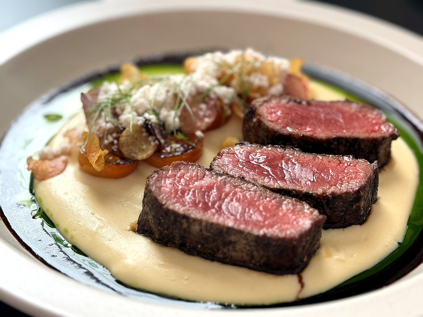 The Holstein ribeye “filet” at Bin 707 Foodbar — rosy sliced medallions over a silky purée with blistered tomatoes, crumbled cheese, and a dark jus ring.