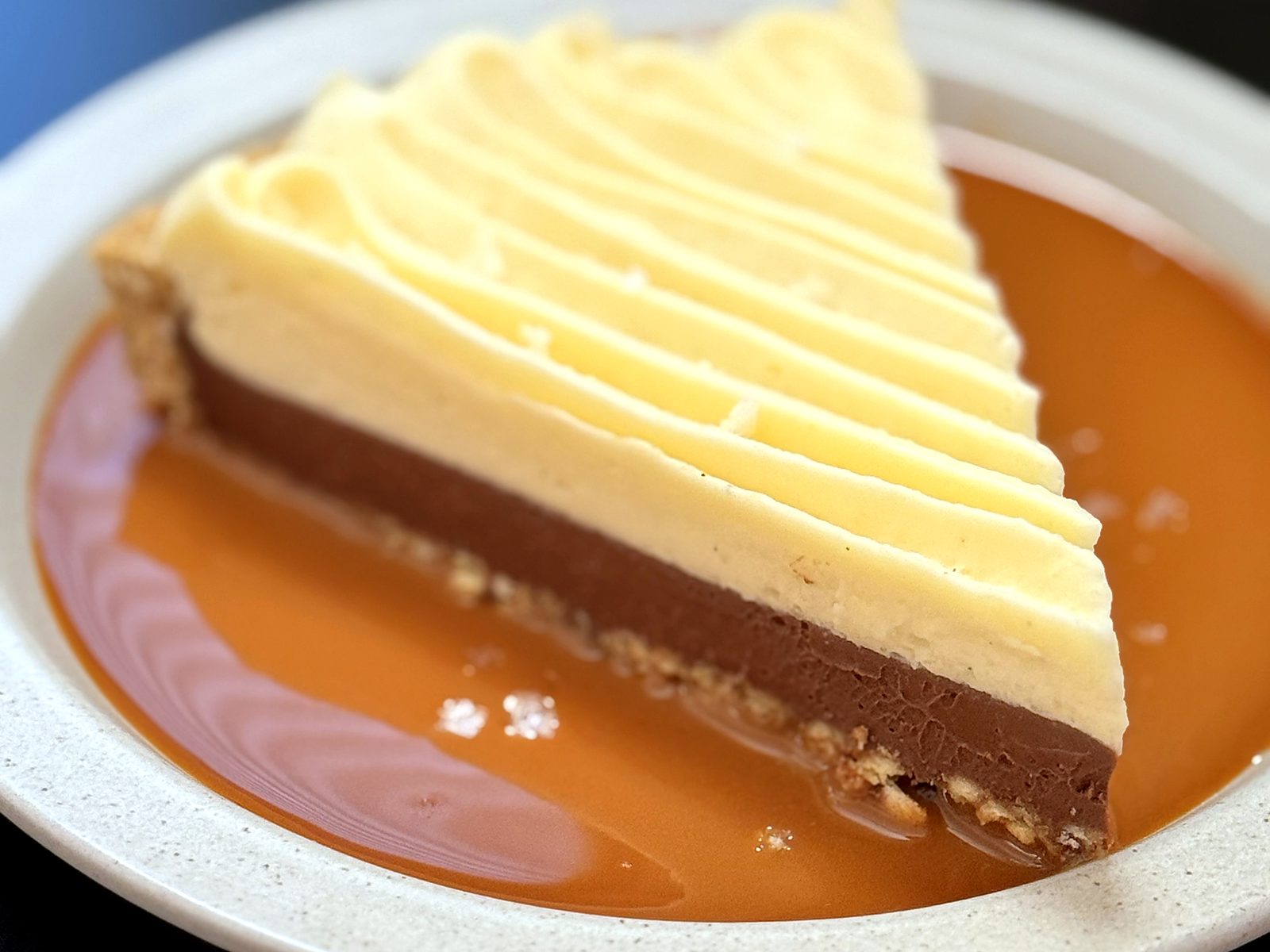 The Momofuku Milk Bar pie at Bin 707 Foodbar — a piped cream-topped wedge over a chocolate layer and cookie crust, sitting in a pool of salted caramel.