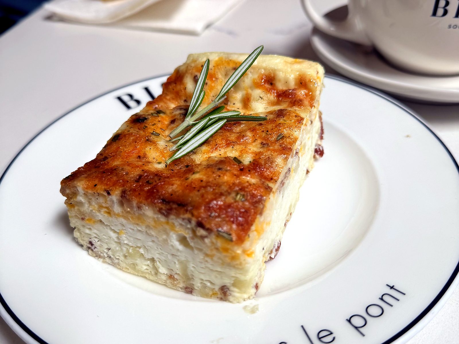 The egg white cocotte at Bisou — a golden-topped baked square with cheese and rosemary on the café’s sous le pont china.