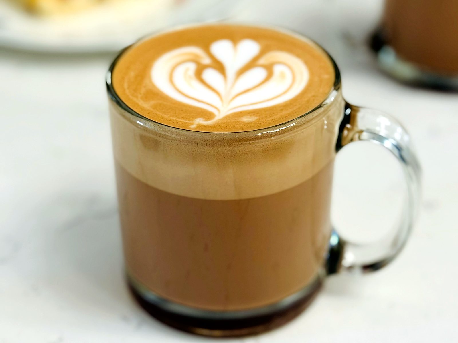 The orange vanilla latte at Bisou, poured with a tulip in a glass mug on the marble counter.