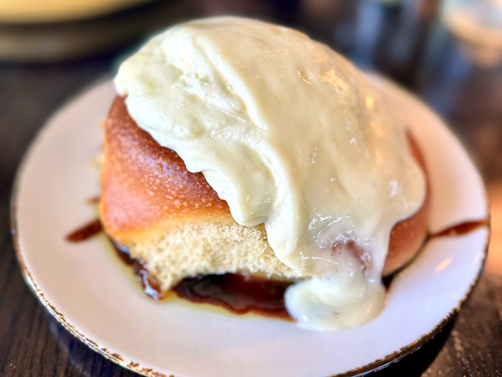 The Sunday brunch cinnamon roll at The Brass Onion — a giant roll under a thick sheet of cream cheese frosting, caramel pooling out from underneath.