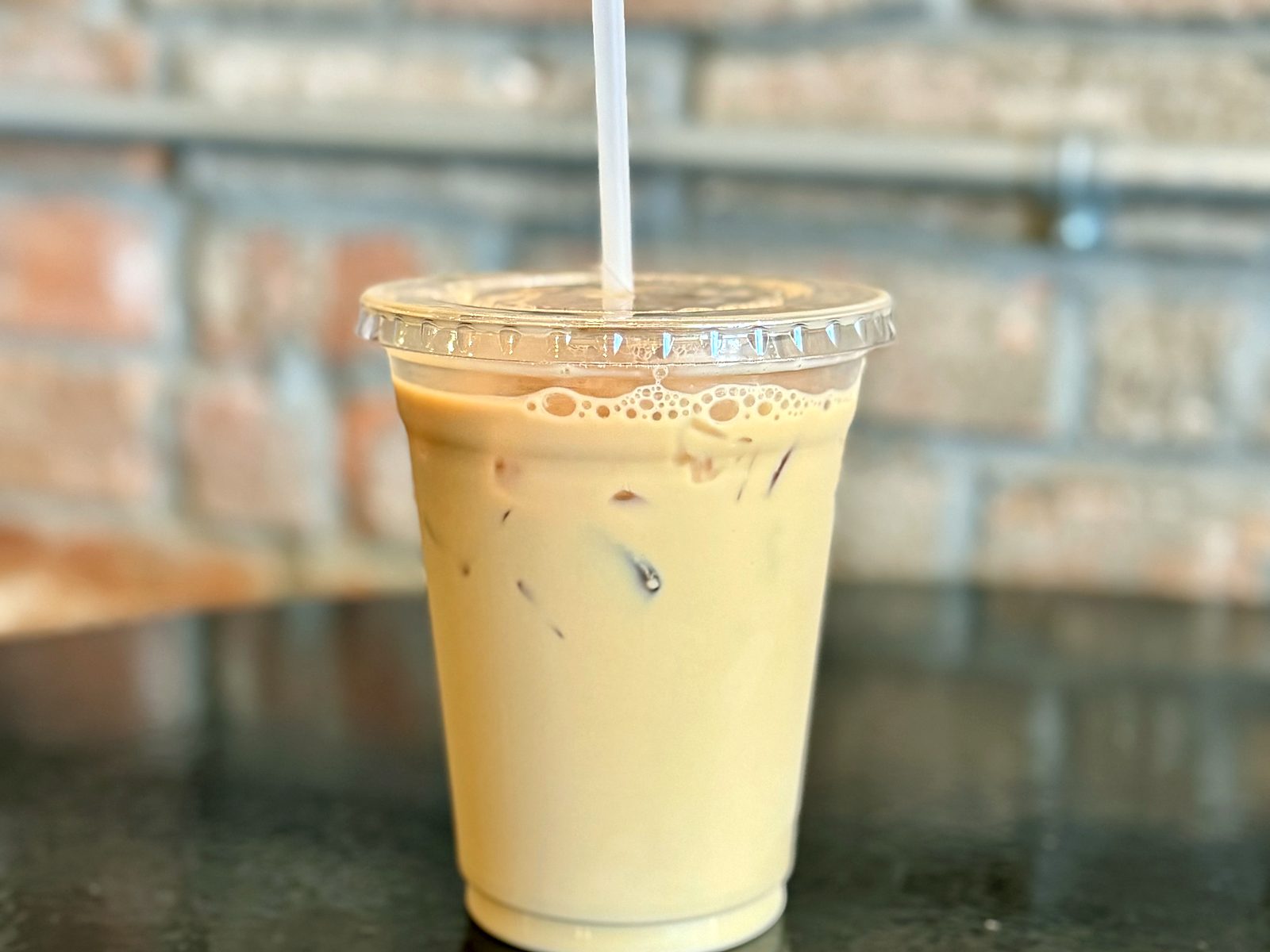 An iced latte at Breathe Coffee House, pale with milk against the café&rsquo;s brick wall.