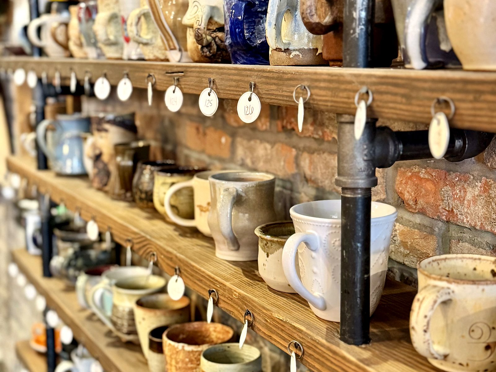 The mug shelves at Breathe Coffee House — rows of handmade stoneware mugs on scaffold-pipe shelving, each hung with its own numbered tag.