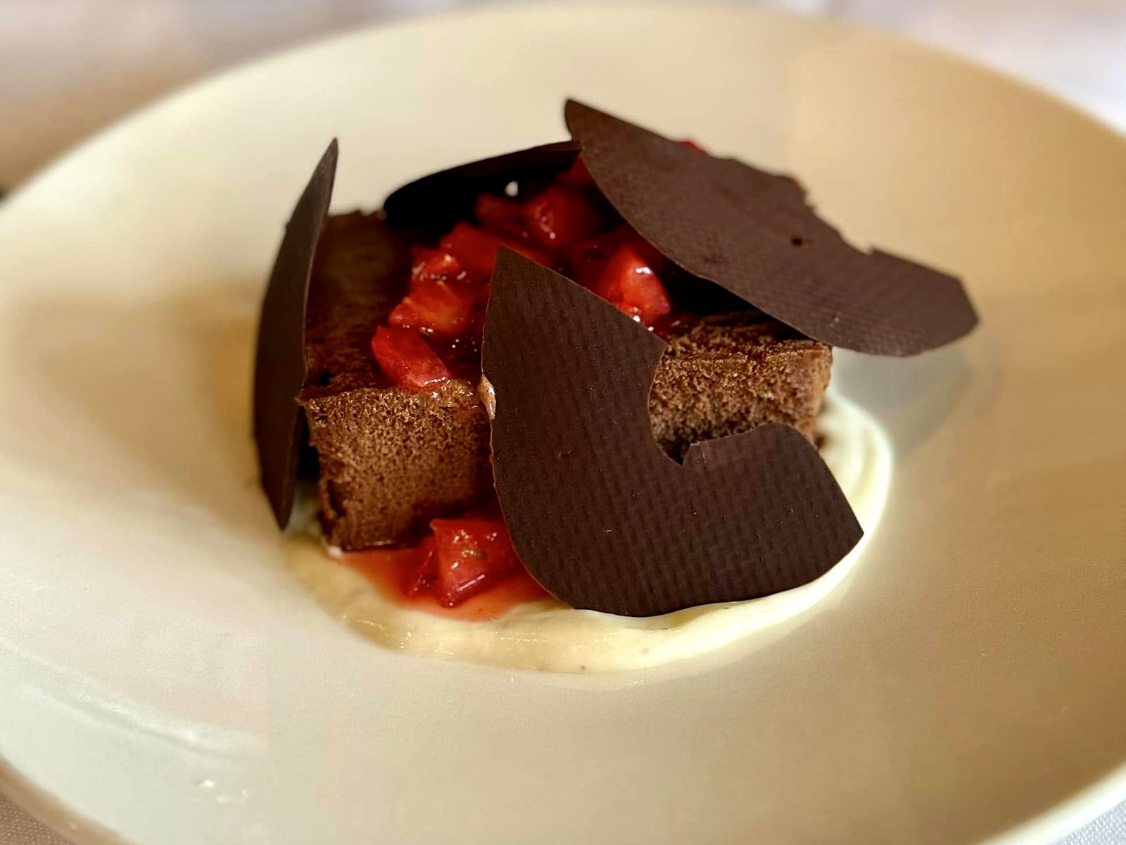 A chocolate dessert at Café Provence — mousse cake with diced strawberries, dark chocolate shards standing upright, on crème anglaise.