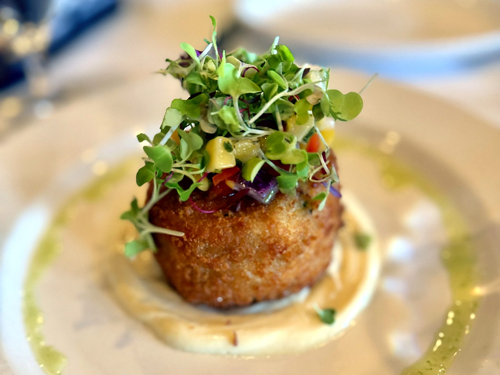 The crab cake at Café Provence — panko-crisped, crowned with microgreens and diced fruit salsa, set on a pool of sauce ringed with herb oil.