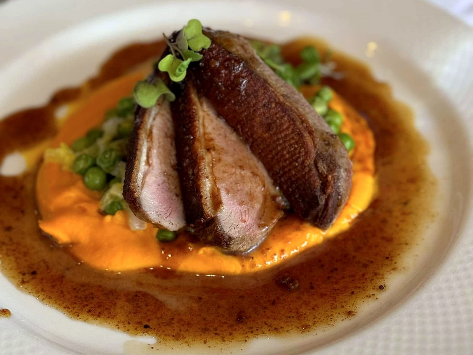 Sliced duck breast at Café Provence — crisp-skinned and rosy, fanned over carrot purée with peas and cabbage in a pool of jus.