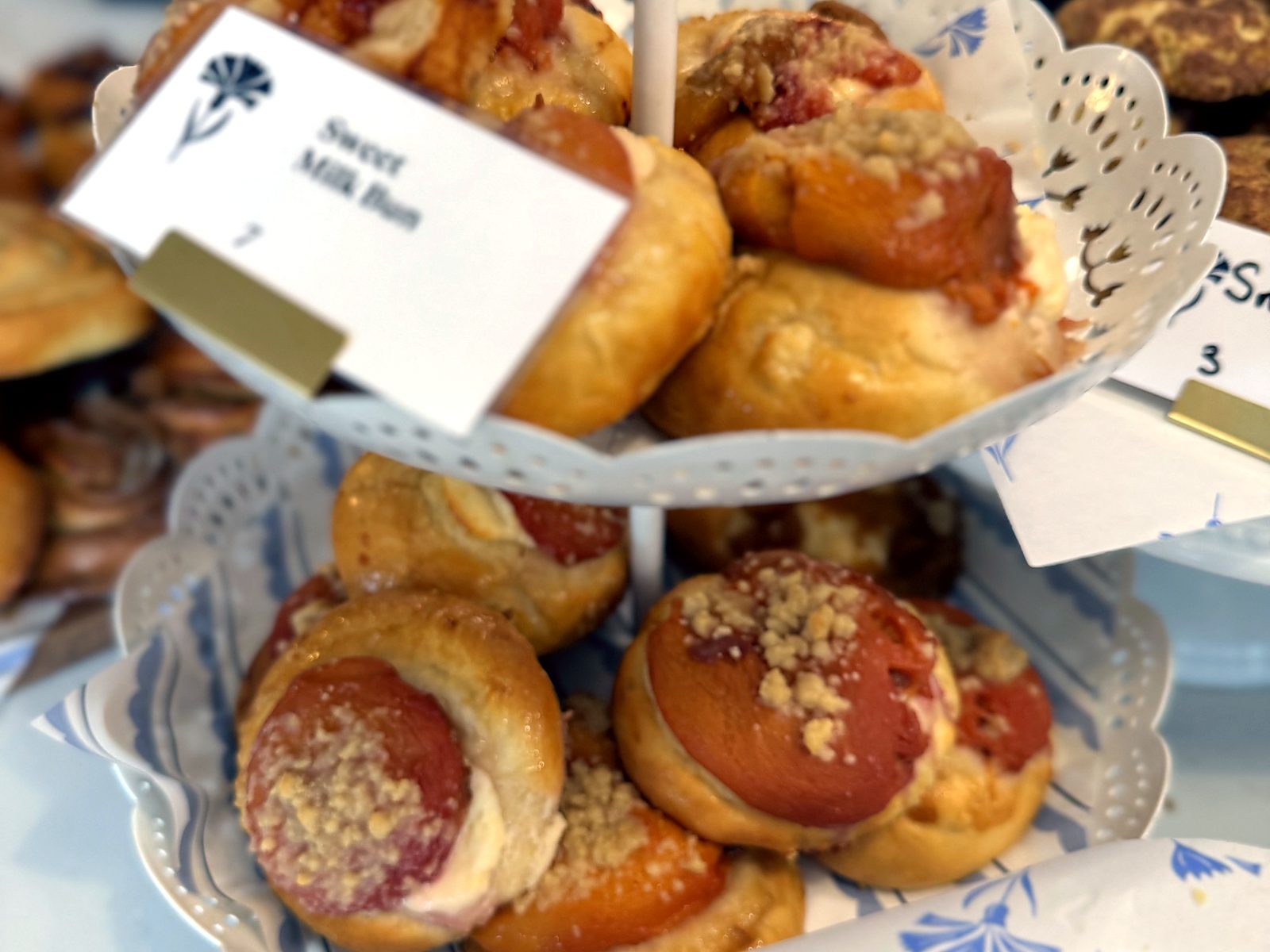 Sweet milk buns at Cornflower Baked Goods — a tiered stand of cream-filled buns under fruit and crumble, the flavor card marked with the cornflower logo.