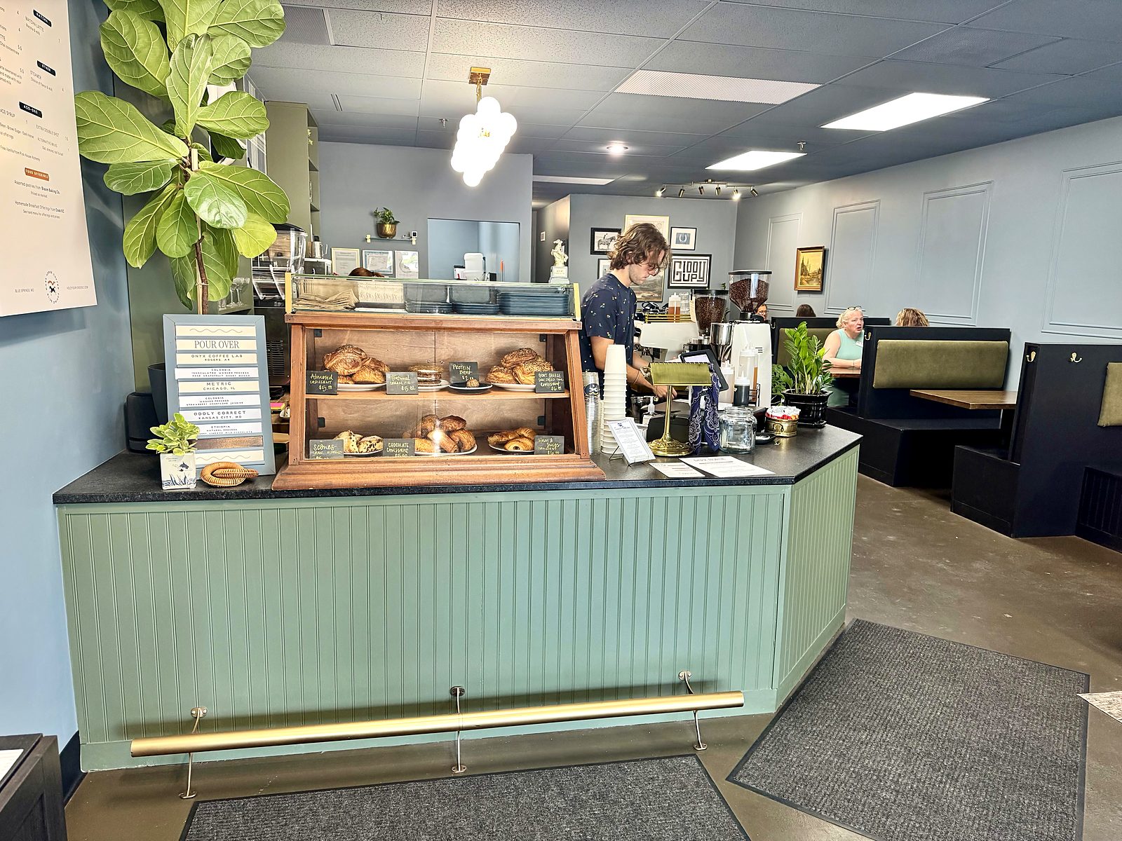 The counter at Dark Horse Coffee — a wooden pastry case of croissants and scones, a barista at the espresso machine, and a card listing the pour-over roasters: Onyx, Metric, and Oddly Correct.