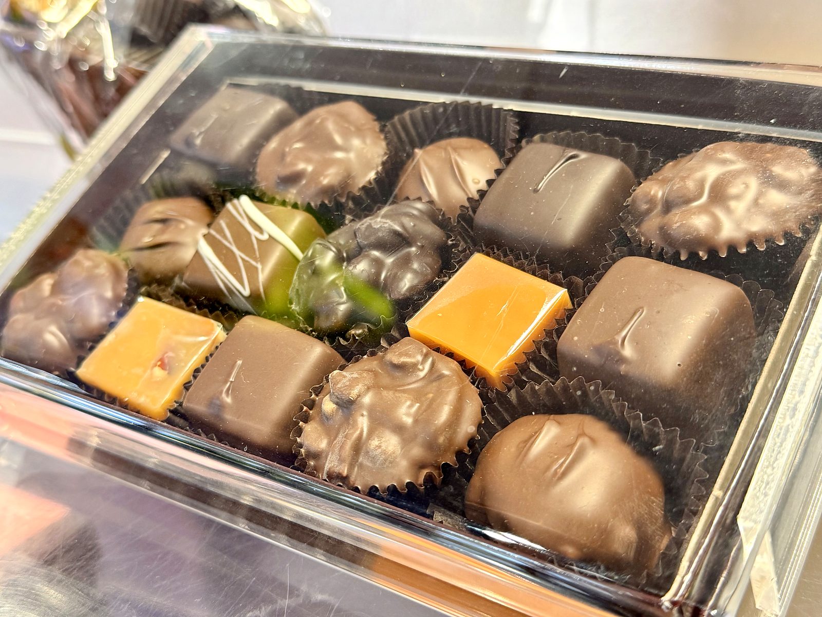 Assorted hand‑dipped chocolates at Enstrom &mdash; milk and dark shells, nut clusters, squares of caramel, and one white‑chocolate drizzle.
