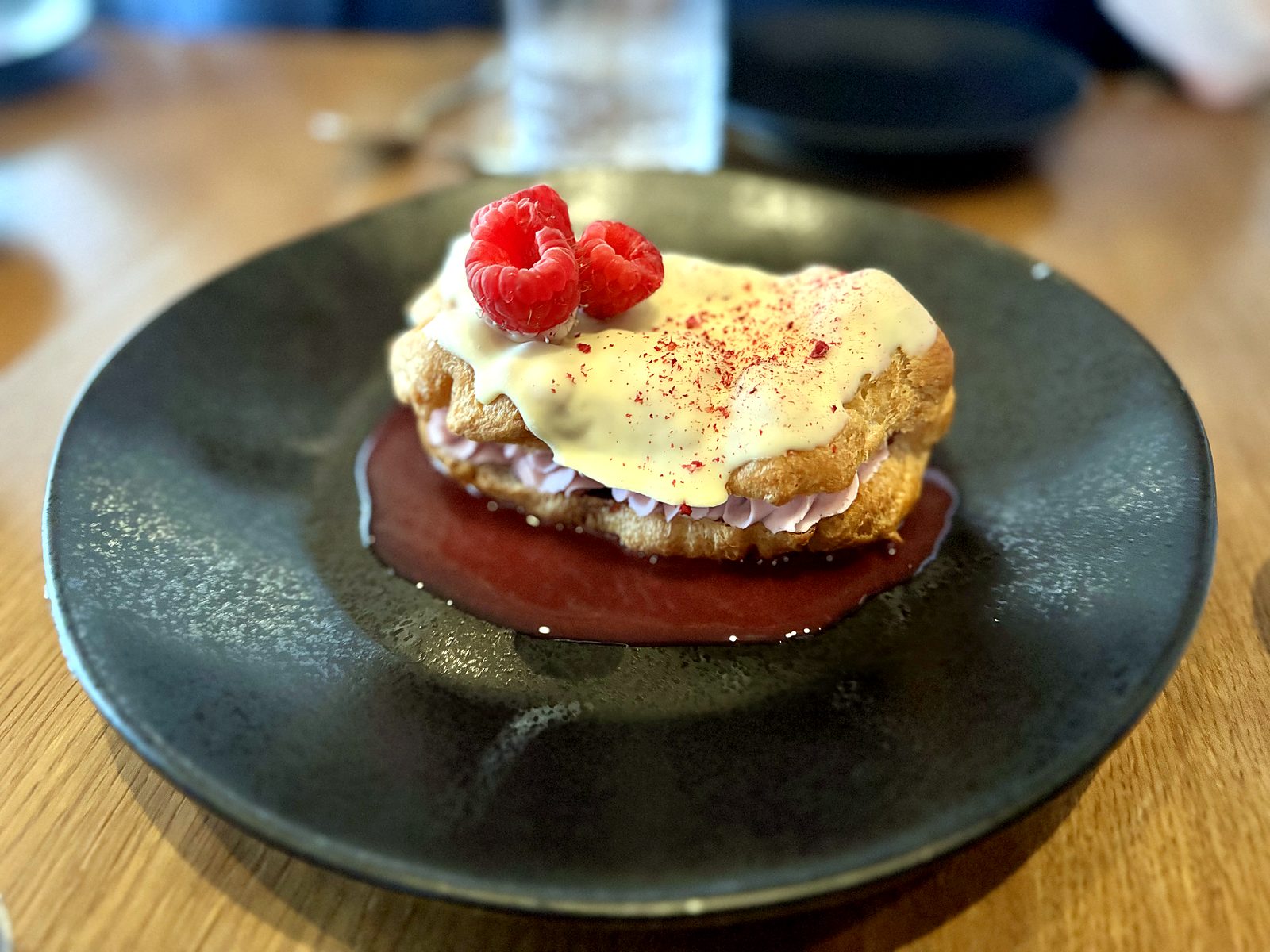 The raspberry éclair at Farina — choux filled with raspberry cream, glazed in white chocolate, topped with fresh raspberries over a pool of berry sauce.