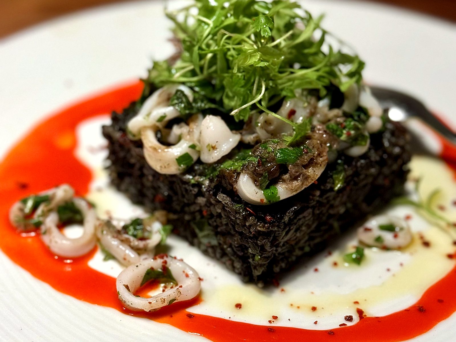 Squid-ink rice at Farina — a pressed black rice cake topped with marinated calamari and herbs, ringed in red pepper sauce.