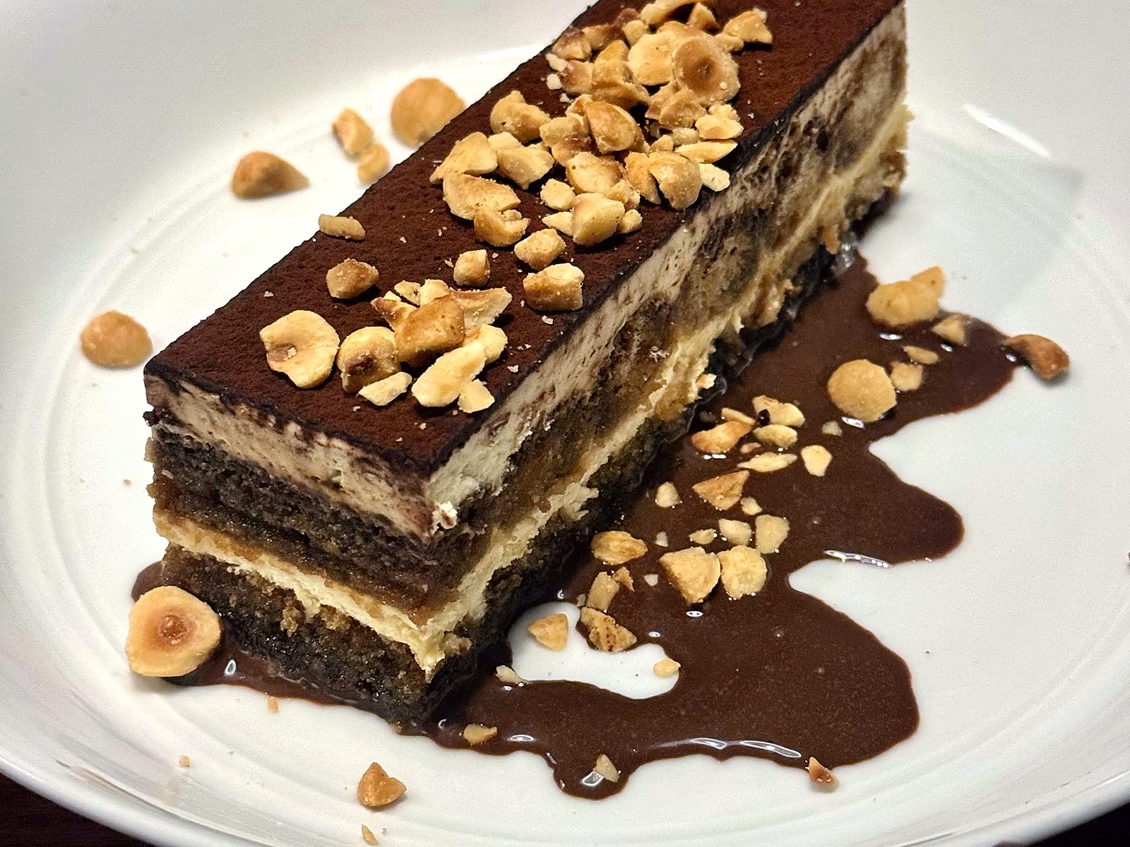 Tiramisu at Farina — a cocoa-dusted layered bar scattered with toasted hazelnuts over a pool of chocolate.