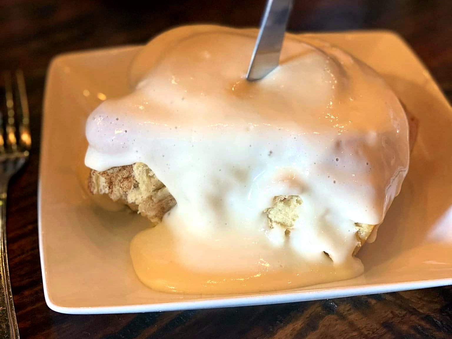 The cinnamon roll at The Farmhouse, buried under a landslide of icing with a knife standing upright in the center.