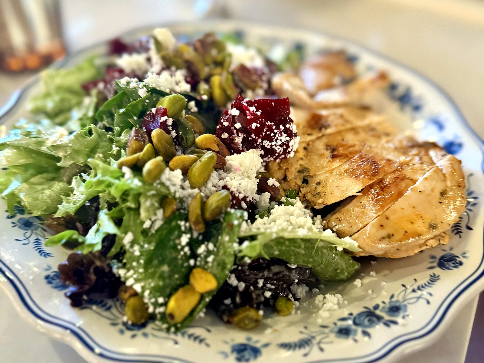 The beet salad with grilled chicken at The French Market — greens, red beets, pistachios, and goat cheese crumbles beside sliced chicken on blue-floral china.