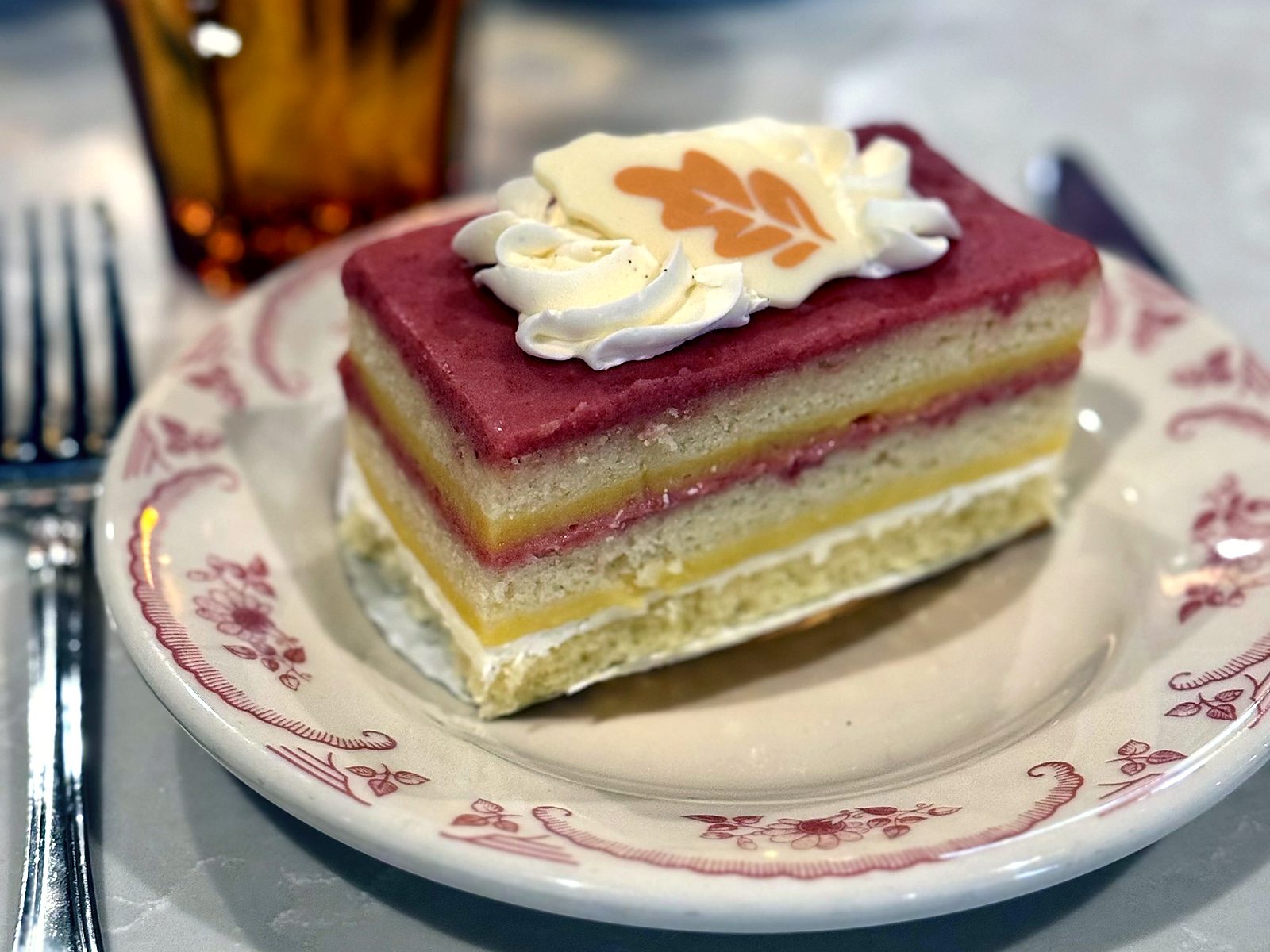 A slice of passionfruit strawberry cake at The French Market — layered sponge, passionfruit curd, and strawberry cream on floral china.