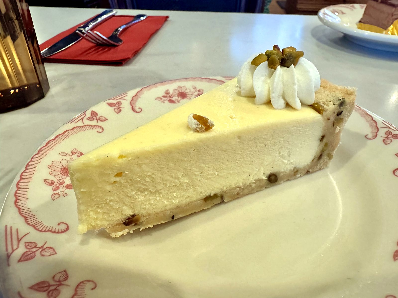 The goat cheese and pistachio cheesecake at The French Market — a pale slice on floral china with a pistachio-studded crust, whipped cream, and chopped pistachios on top.
