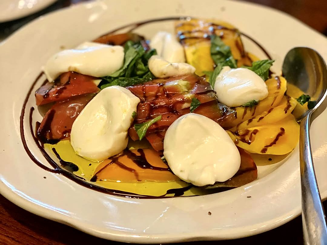 The tableside mozzarella caprese at Jasper's — folds of just-made mozzarella over red and yellow heirloom tomatoes and basil, ringed with balsamic and olive oil.