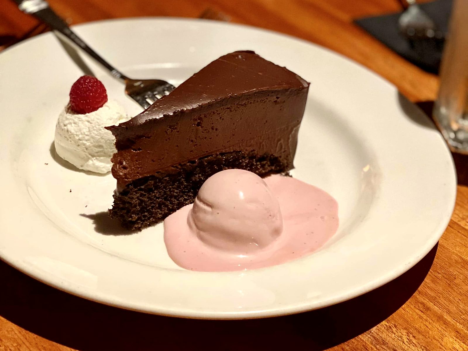 Chocolate mousse cake at J. Gilbert's — a ganache-topped slice beside raspberry cream and a raspberry-crowned dollop of whipped cream.