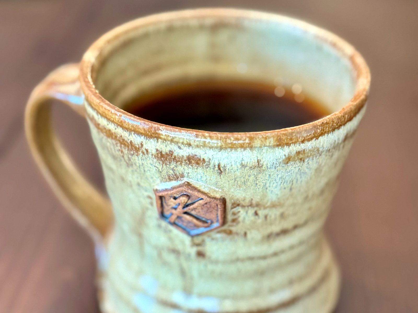 Black coffee at Kiln Coffee Bar in a handmade stoneware mug, glazed sand and rust and stamped on the side with a hexagonal K.