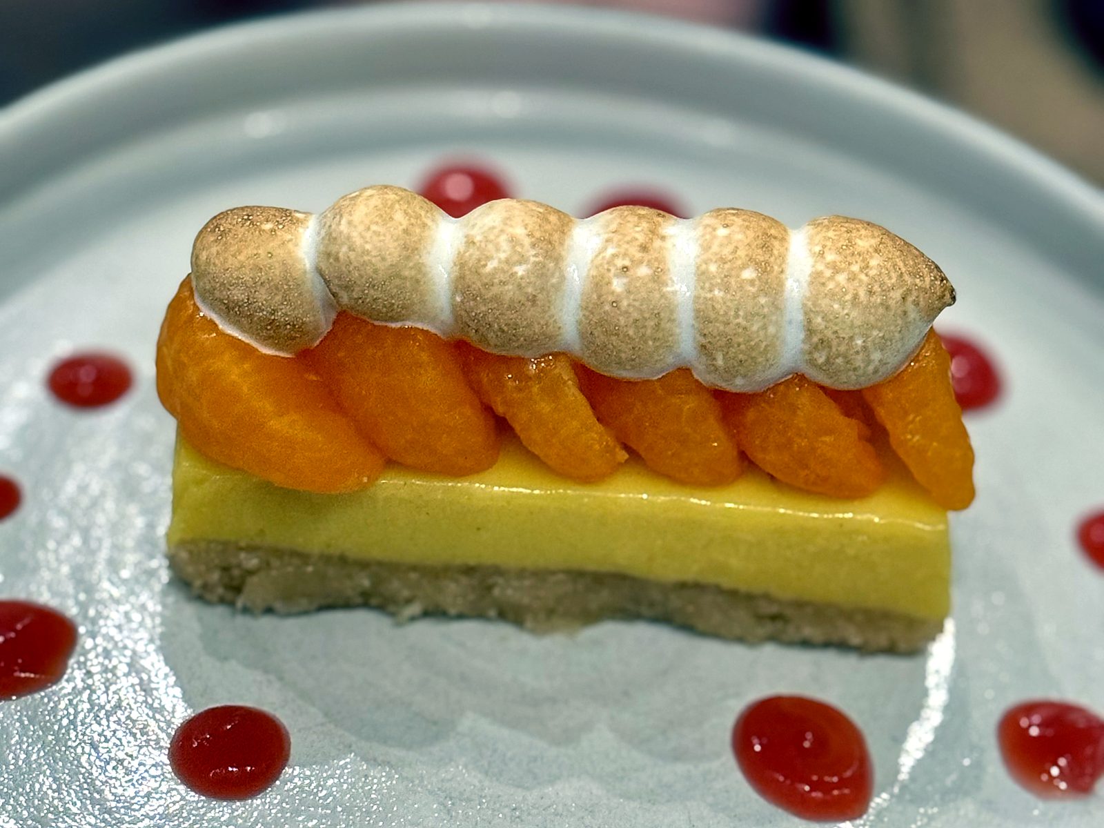 A citrus tart at Lazia — shortbread crust, curd, glazed citrus segments, and a torched rope of meringue, ringed with red fruit gel.