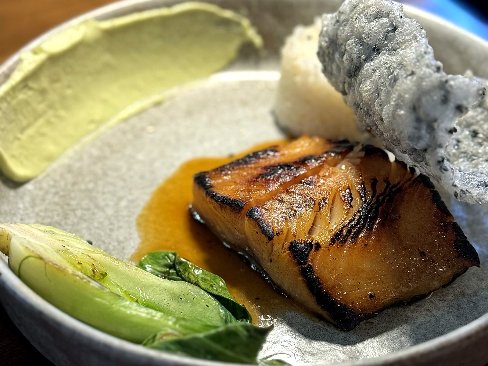 Miso cod at Noka — charred glazed fillet over rice with a puffed sesame rice cracker, baby bok choy, and a swipe of green purée.