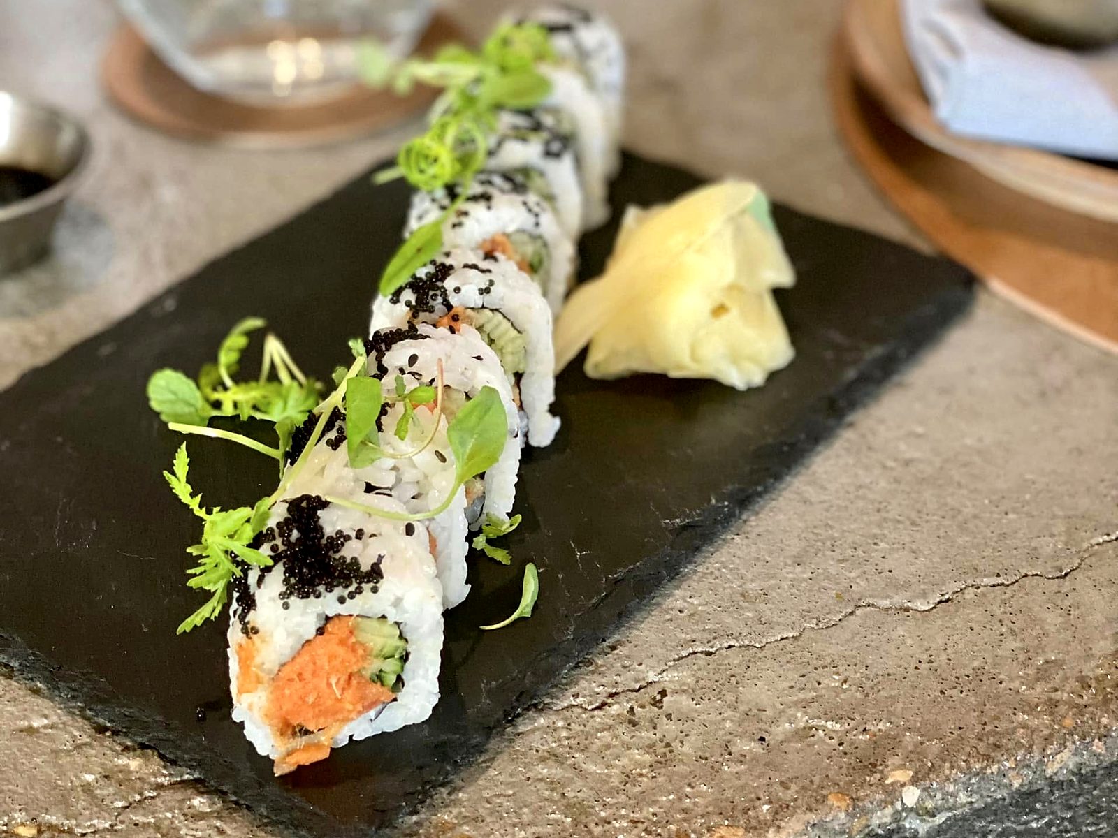 A spicy tuna roll at Noka — cut pieces under black tobiko and micro herbs, pickled ginger alongside.