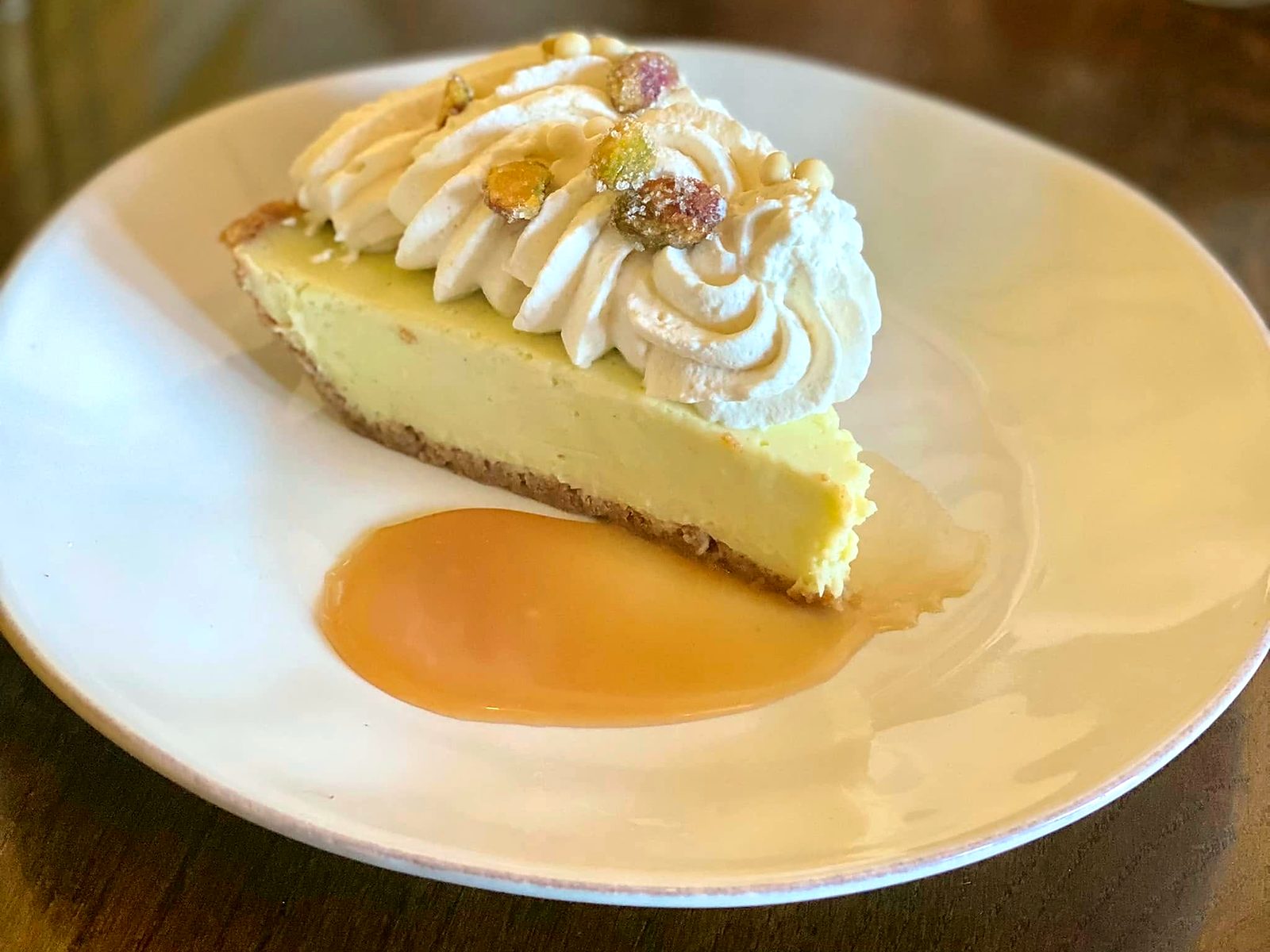 A cream pie at Novel — silky custard on a crumb crust under piped whipped cream and candied pistachios, a pool of caramel alongside.