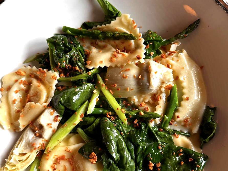 The ricotta ravioli at Novel — house-made pasta stuffed with ricotta, mascarpone, and Parmesan, tossed with local asparagus and spinach under a scatter of crispy garlic.
