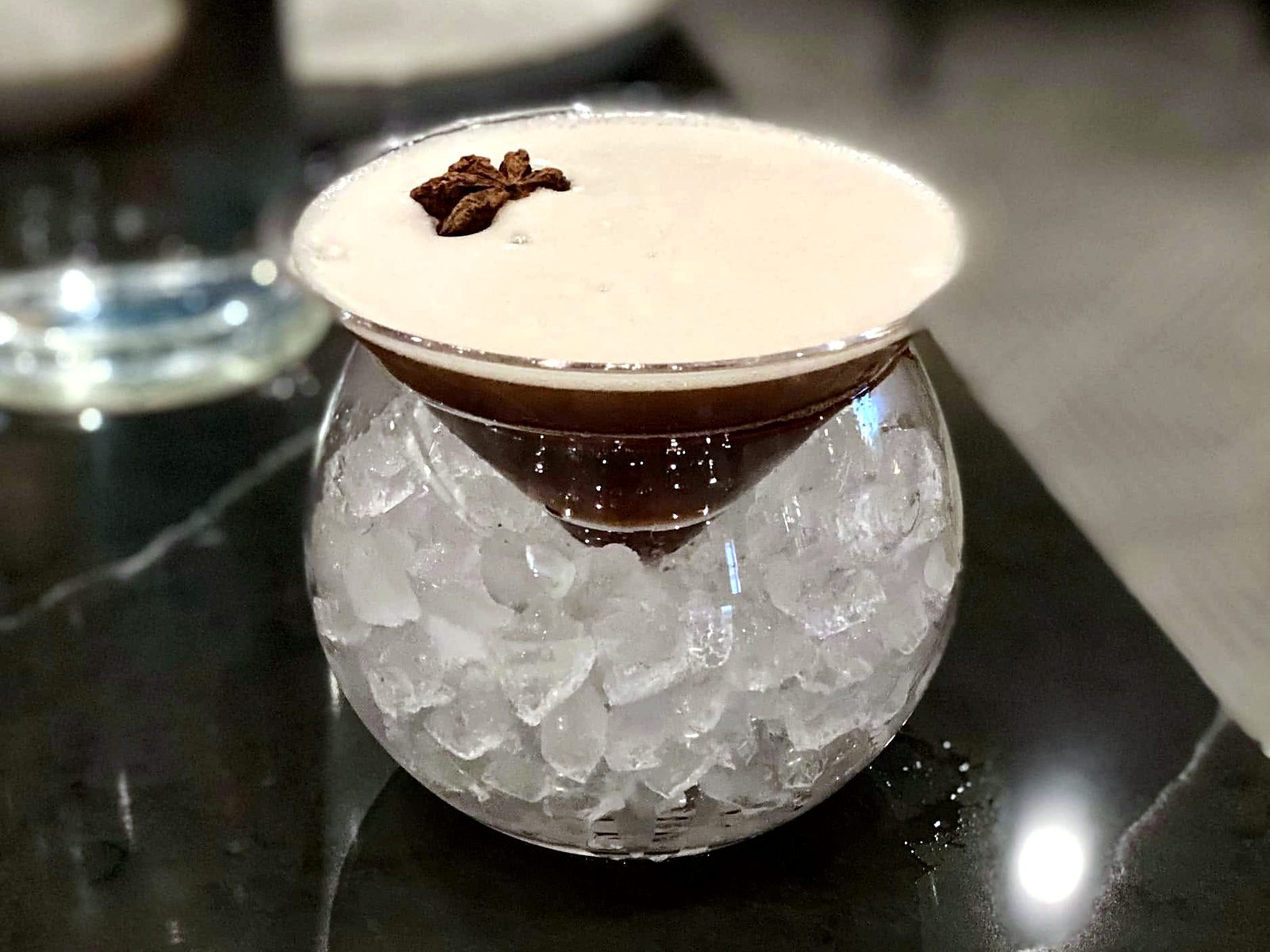 The espresso martini at Of Course Kitchen & Company — served in a cone glass nested in a sphere of crushed ice, star anise floating on the foam.