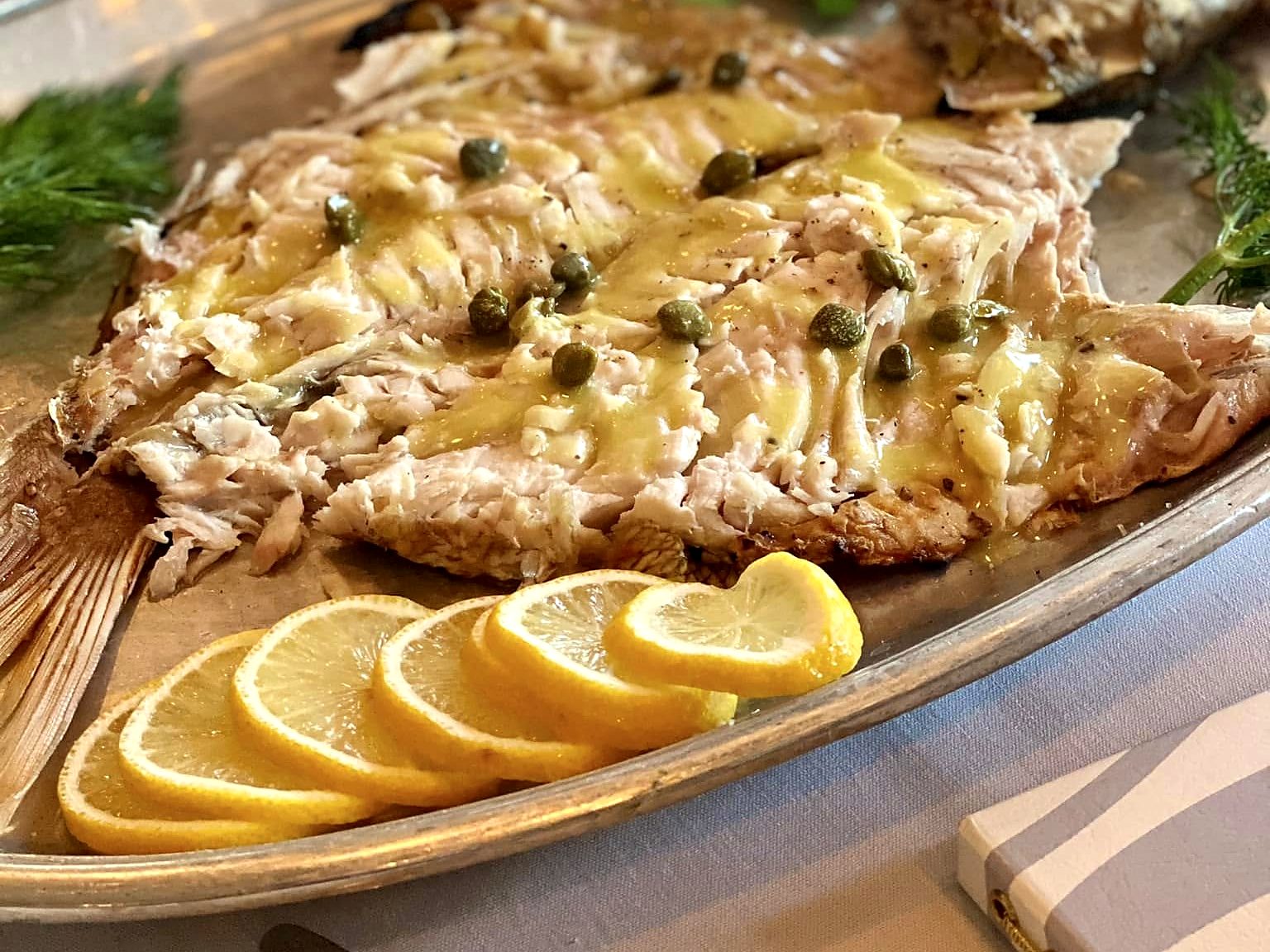 The salt-crusted branzino after the reveal at Paros — filleted tableside, dressed with capers and lemon oil, lemon slices fanned alongside.