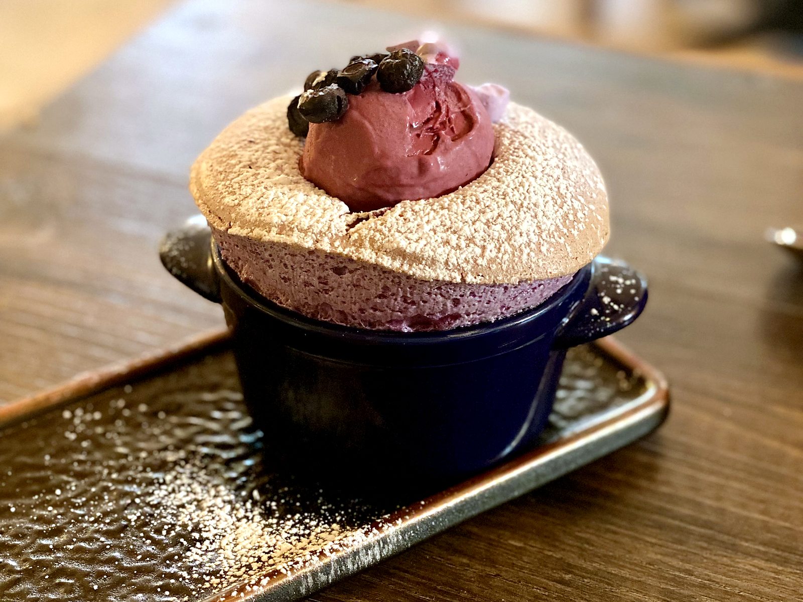 The blueberry soufflé at Pêche — risen and sugar-dusted in a blue cocotte, with blueberry ice cream melting into its center.