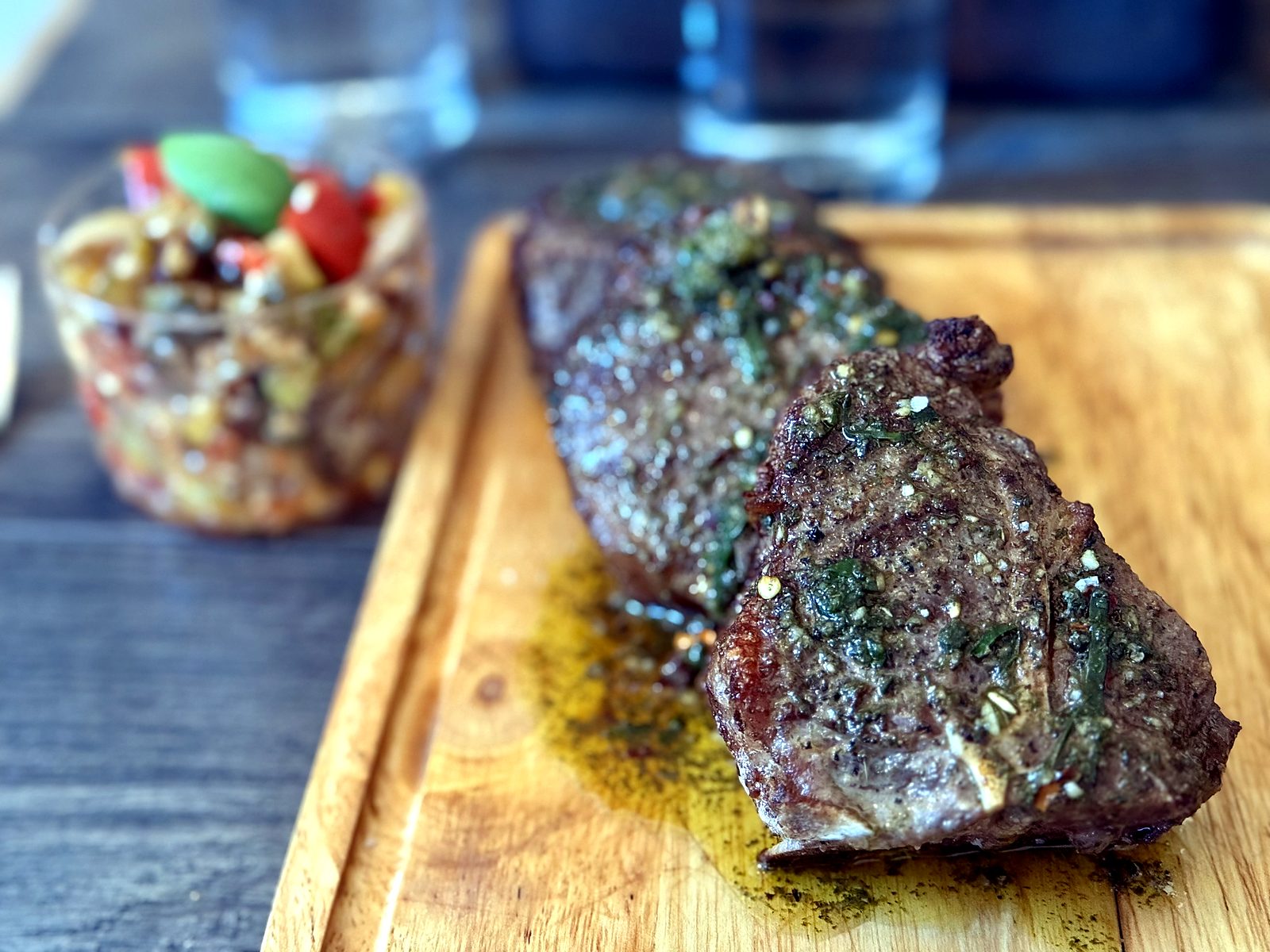 Lamb t-bones at Pêche, herb-crusted on a wooden board with green sauce pooling beneath and a relish cup behind.