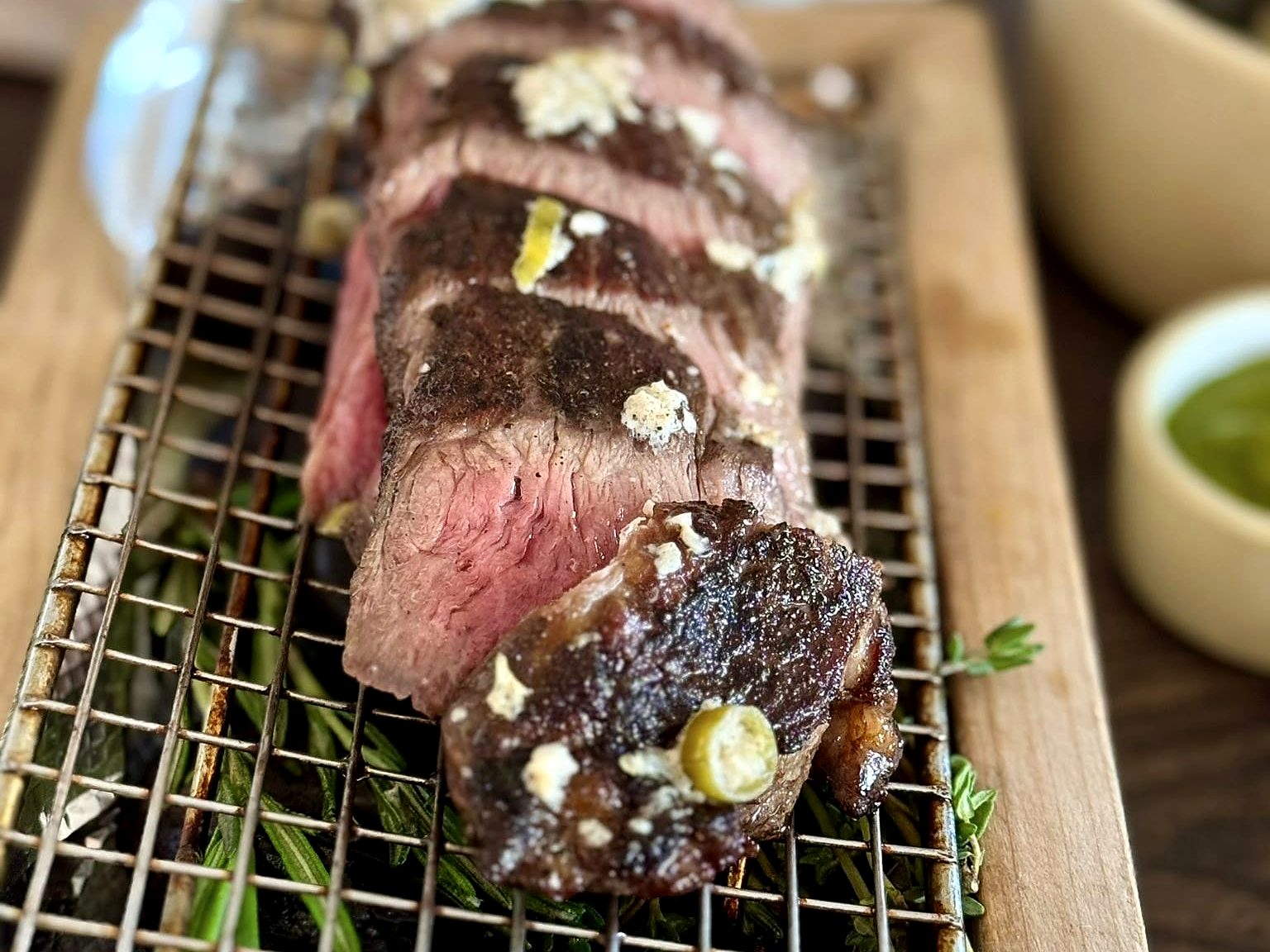 Sliced ribeye at Pêche — fanned rosy slices under melting compound butter, set over smoking rosemary and thyme.
