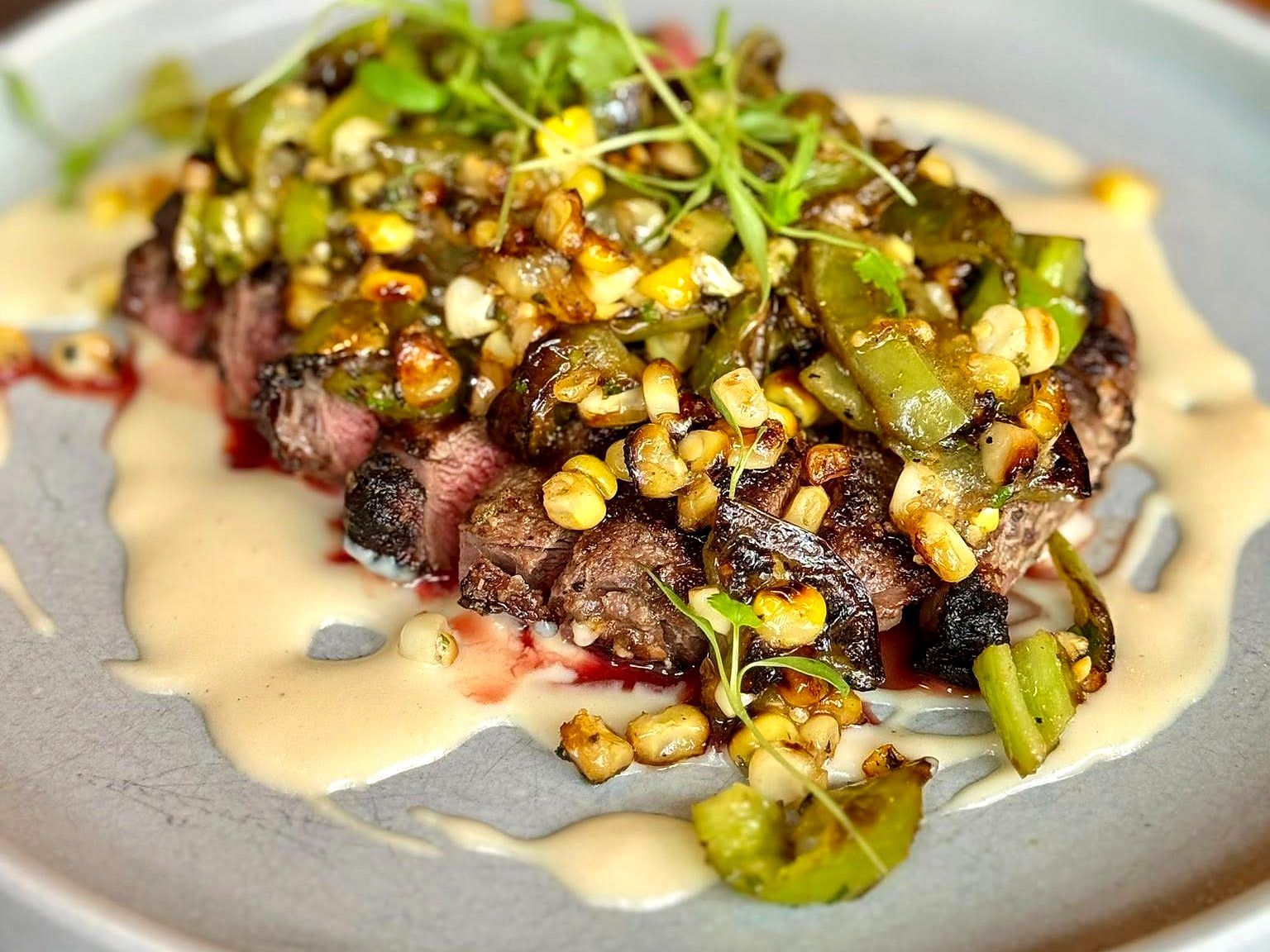 Sliced steak at The Pullman — charred and rosy under a heap of blistered corn and green chiles, over a swirl of crema.