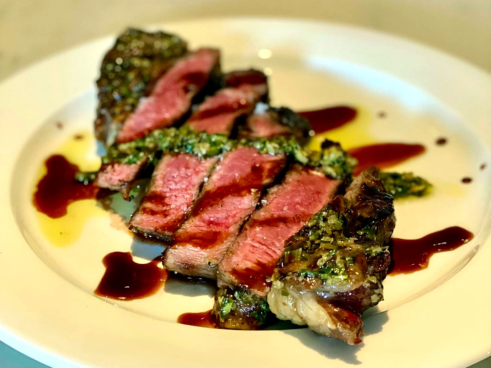 The KC strip at The Restaurant at 1900 — rosy slices under an herb crust with red-wine jus and olive oil dotting the plate.