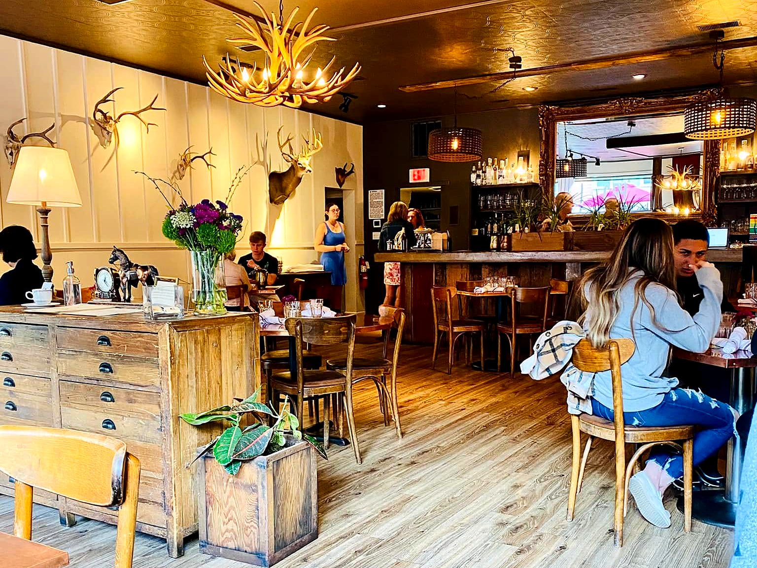 The dining room at CO. Ranch House — antler chandelier, mounted deer, a gold ceiling, and a small bar, all in one snug storefront room.
