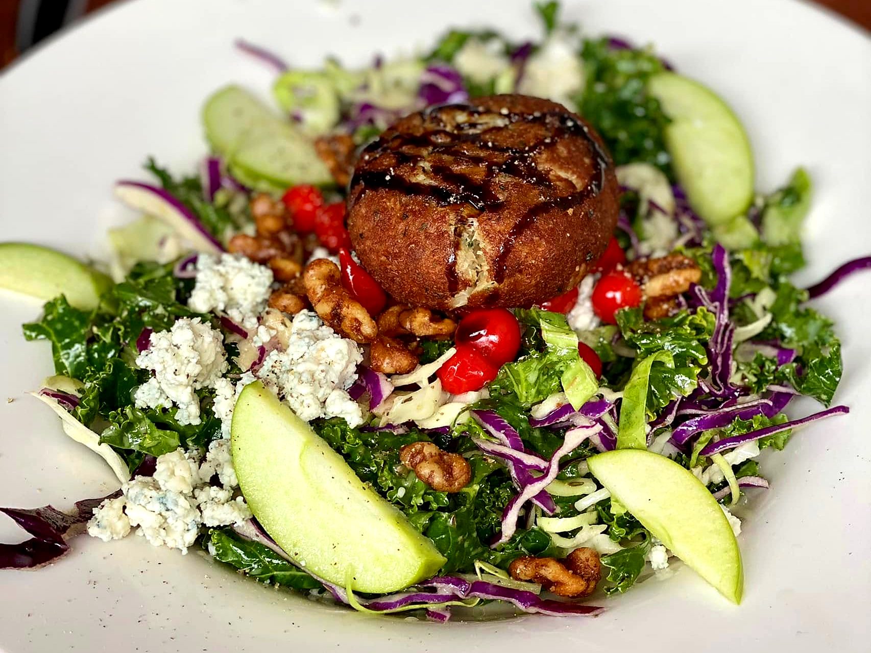 A salad at CO. Ranch House — kale and cabbage with blue cheese, green apple, candied walnuts, and peppadews around a fried cheese round drizzled with balsamic.