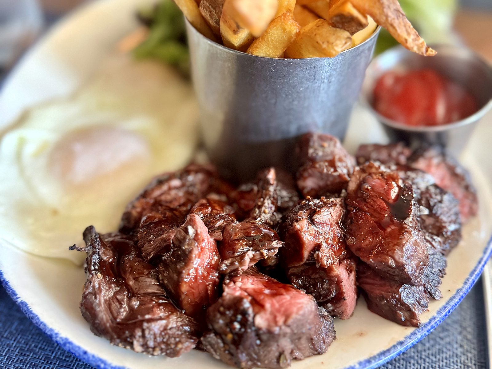 Steak and eggs at Rye — glazed hanger steak tips beside sunny-side eggs, fries, and ketchup.