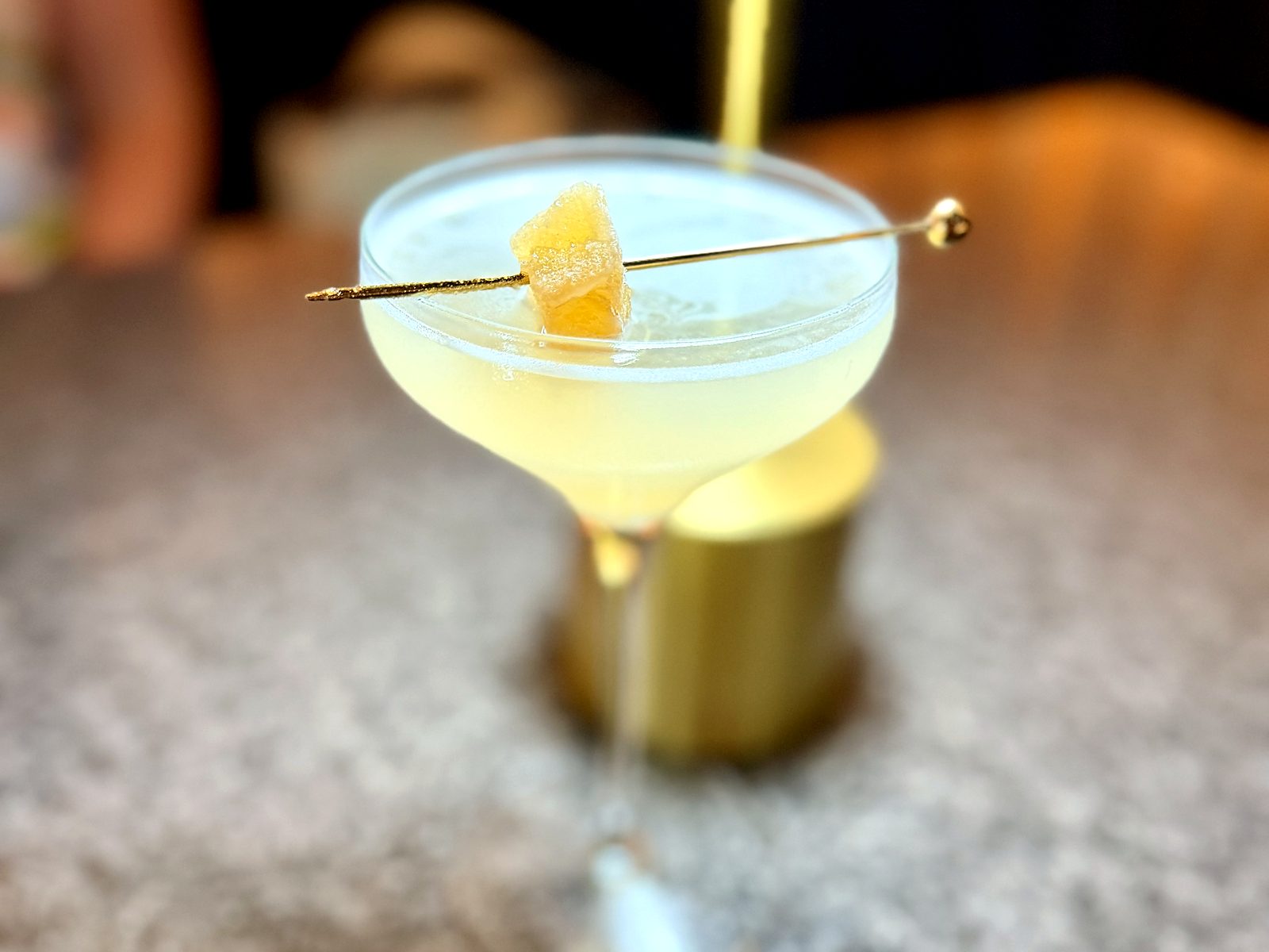 A cocktail at Scratch — a pale coupe garnished with candied ginger on a gold pick.