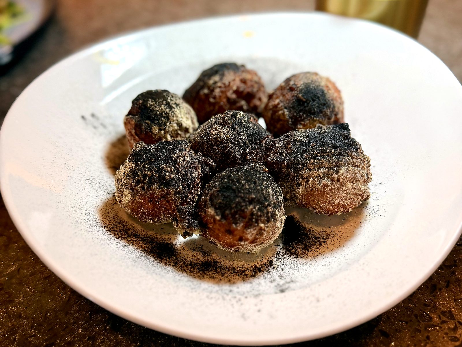 Dessert at Scratch — a plate of fried dough dusted dark with cocoa and sugar, powder drifting across the rim.