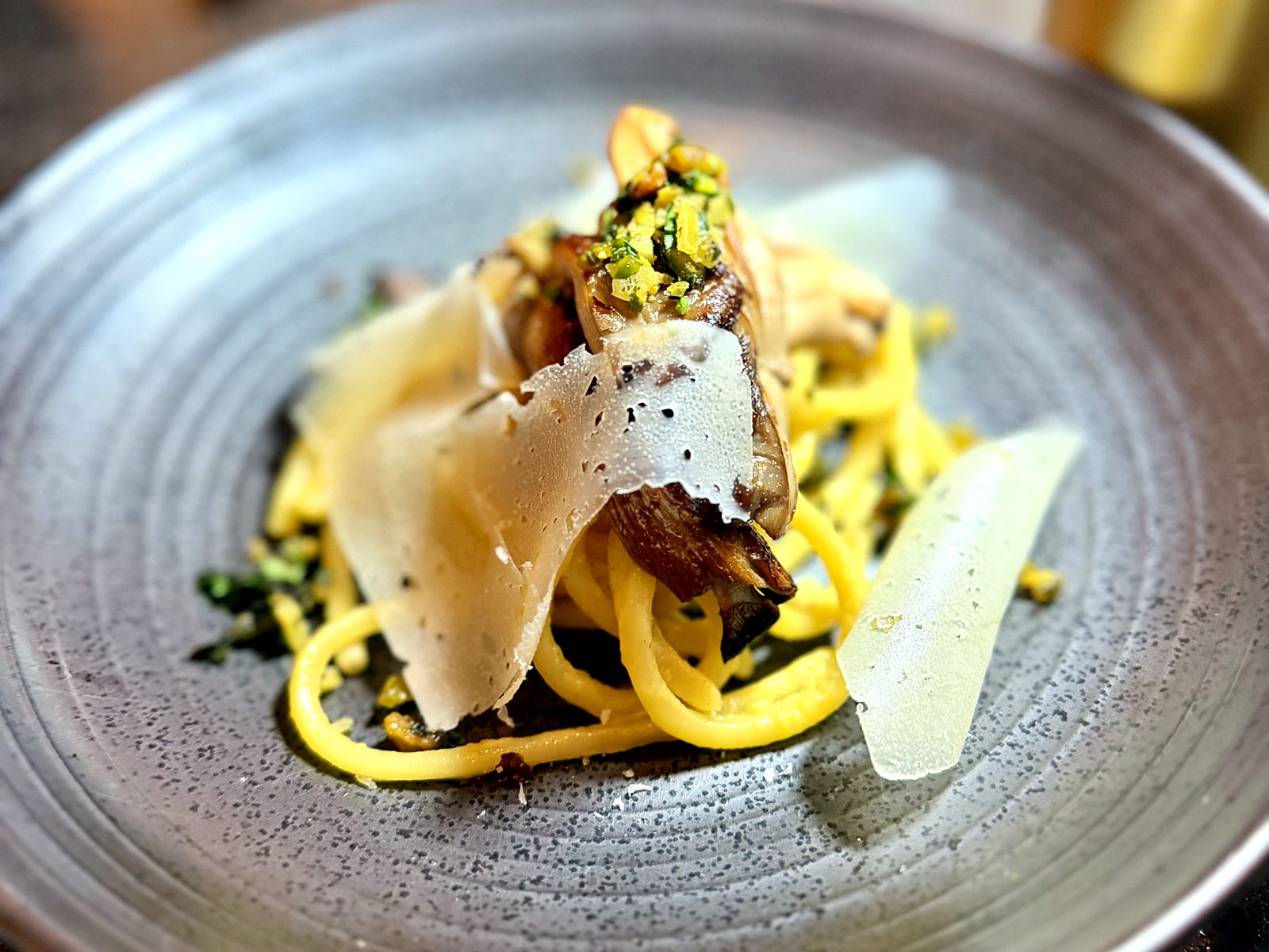 House pasta at Scratch — golden noodles twirled under roasted mushrooms, a green herb crumble, and wide shavings of cheese.