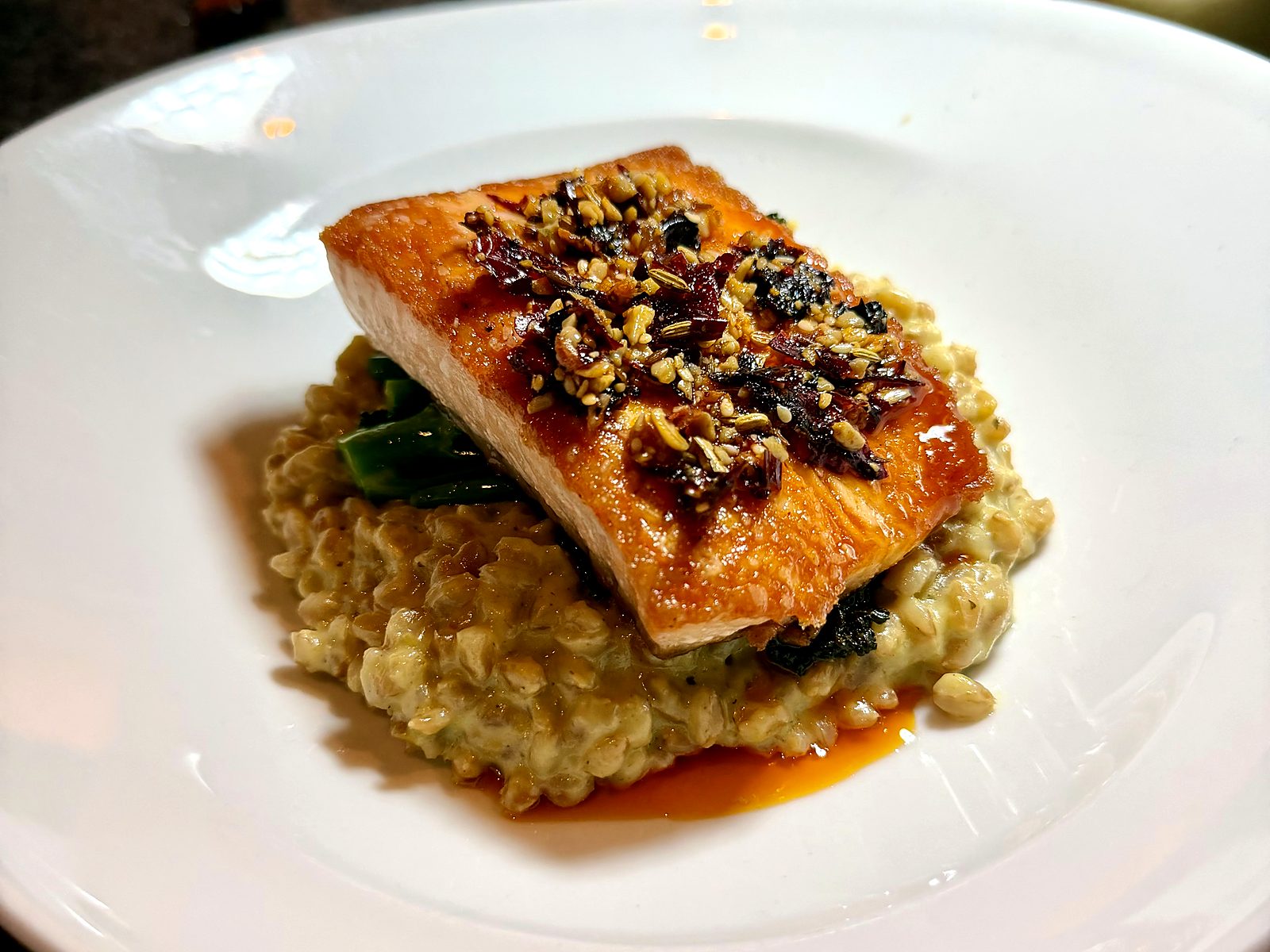 Glazed salmon at Scratch — a crisp-skinned fillet over creamy grain risotto and broccolini, topped with chile crisp, chili oil pooling at the edge of the bowl.