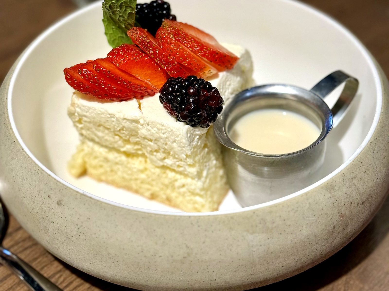 Tres leches at T’ähä — a cream-topped square with strawberries, blackberries, and mint, beside a small pitcher of milk for pouring.