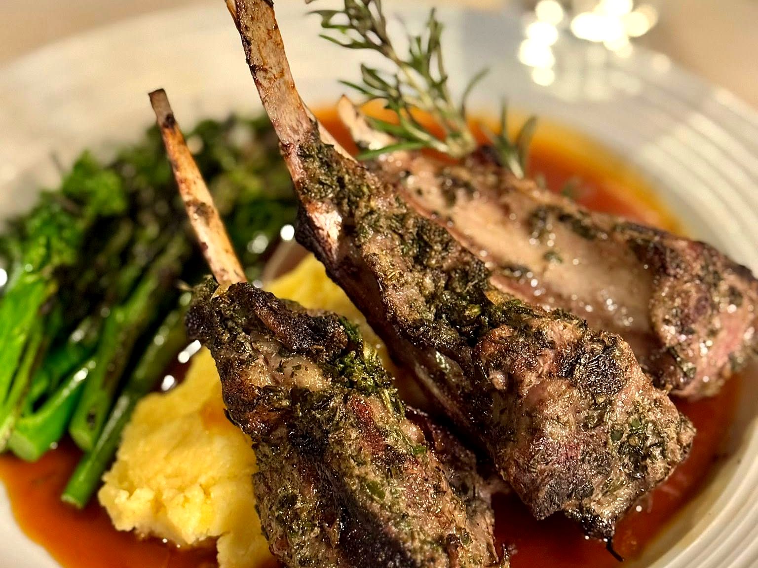 Herb-crusted lamb chops at Tailleur — bones crossed over polenta and charred broccolini in a pool of jus, rosemary standing upright.