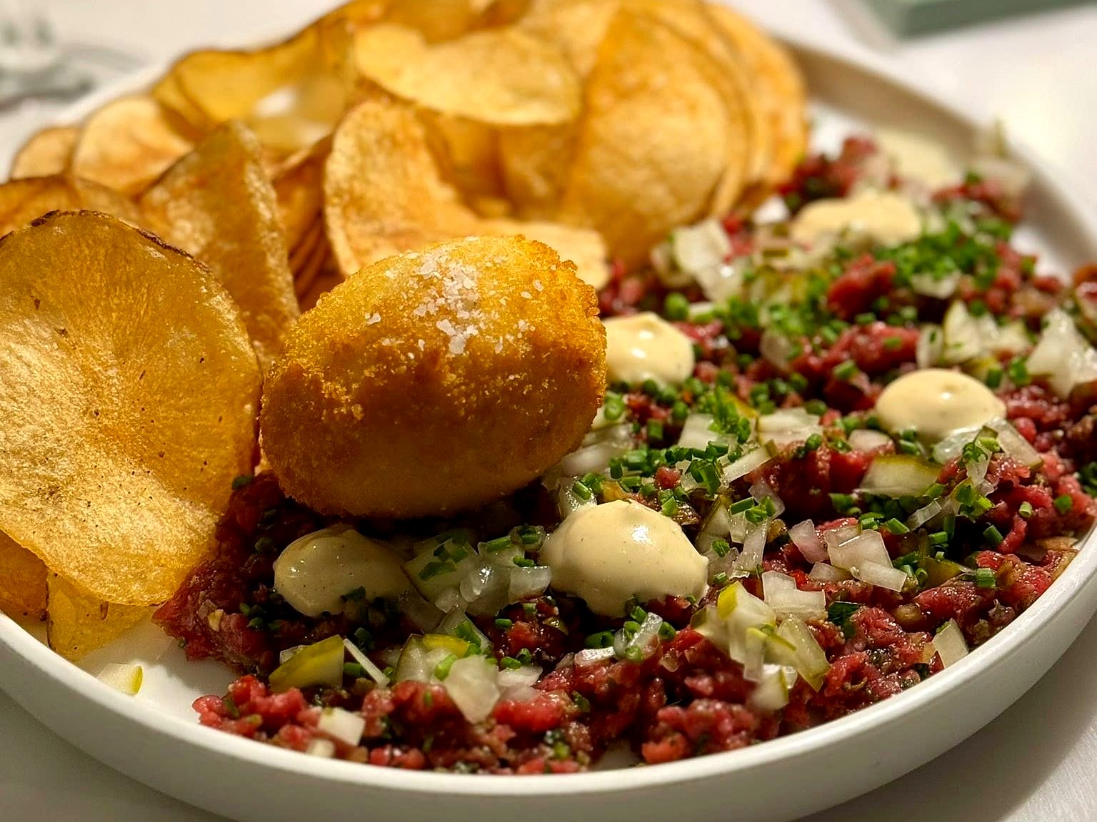 The beef tartare at Verbena — hand-chopped tenderloin with dijonnaise, pickles, and chives, a crispy egg on top and house potato chips piled behind.