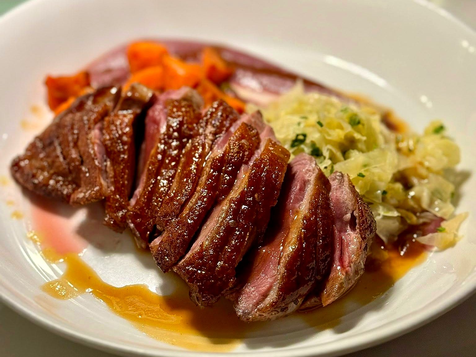 Sliced duck breast at Verbena — lacquered skin and a rosy center, with glazed carrots and buttered cabbage alongside.